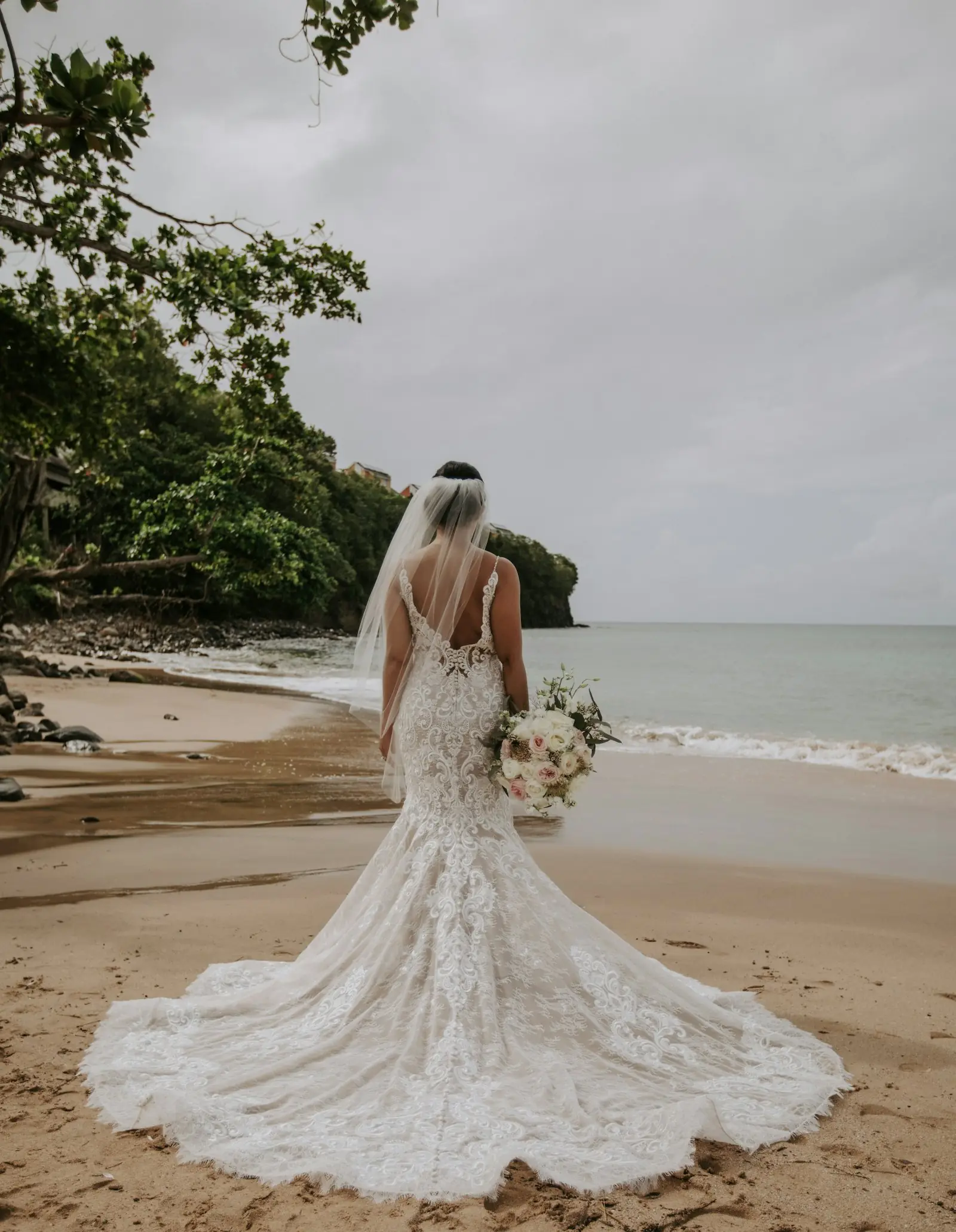 Bride in a lace gown on a beach at the forest edge