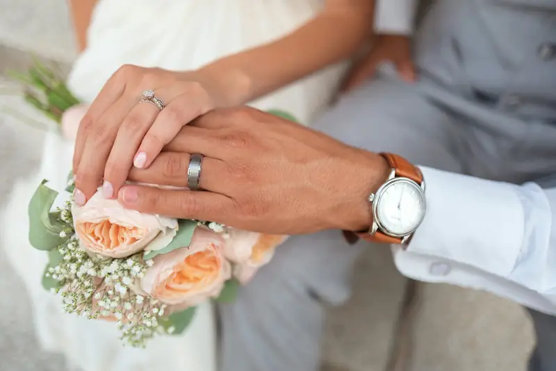 Groom's hand resting on the bride's hand and bouquet